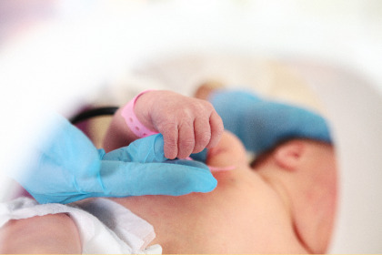 Close up photo of a baby's hand grasping a hand covered by a blue surgical glove.