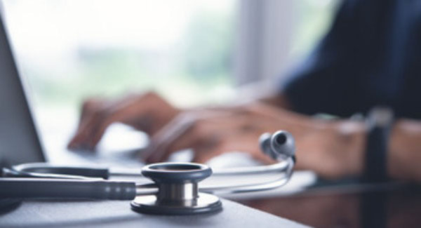 typing on computer keyboard with stethoscope in the foreground