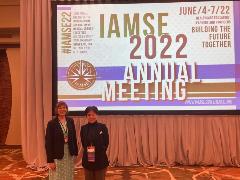 Two people stand in front of a screen for the IAMSE meeting