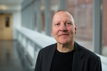 Markus Thali  In a dark jacket, smiling, standing in a hallway with glass wall behind him