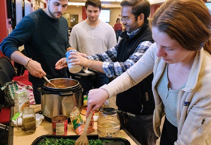 Four people in a classroom, seasoning and stirring soup and sauteeing kale