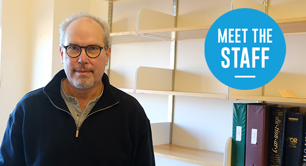 Photo of Owen Nadeau with bookshelves behind him, with a blue circle that says 