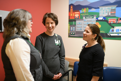 Three people standing in a colorful medical exam room talking and gesturing.