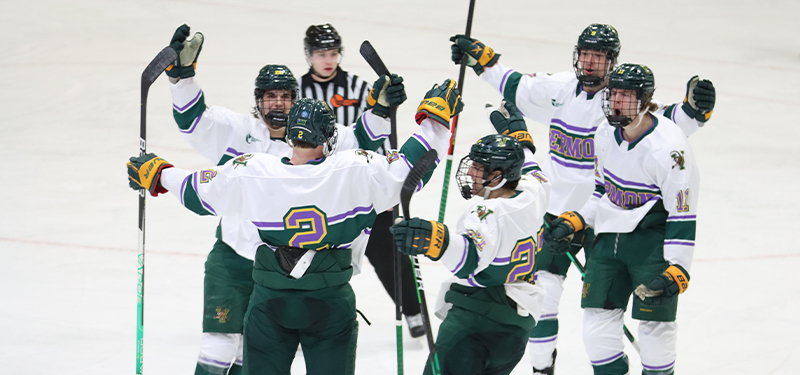 UVM hockey players in rally against cancer jerseys celebrating after a goal.